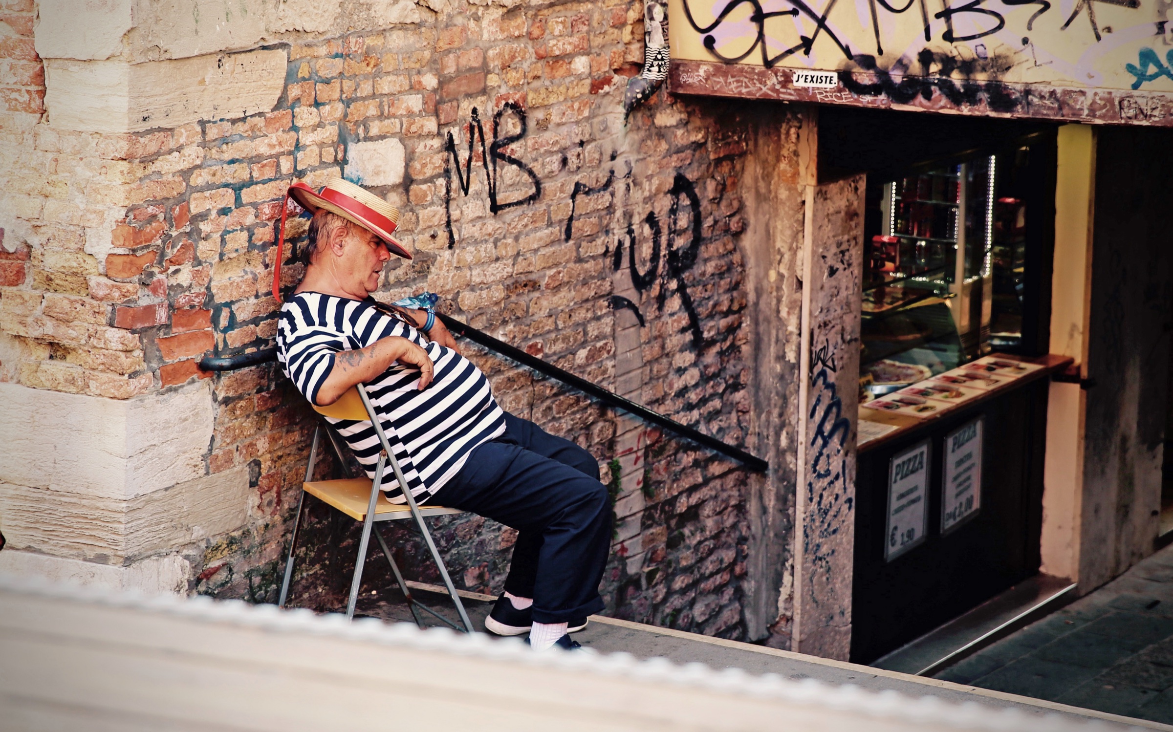 A man in a striped shirt sleeping in a chair on an Italian street