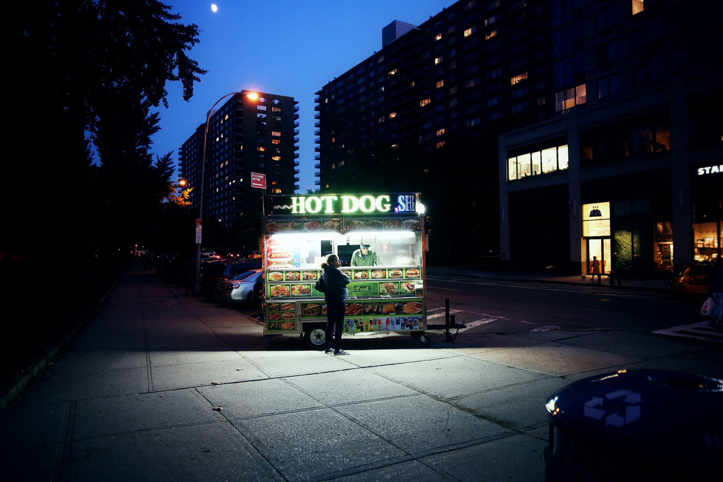 An illuminated hot dog cart on a dark New York City street