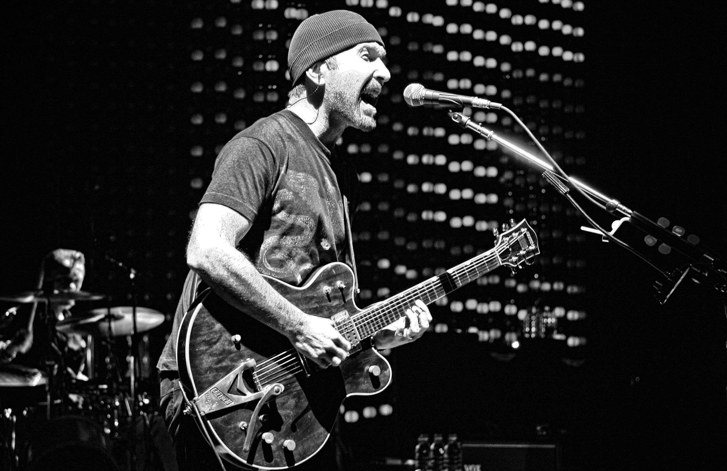 The Edge of U2 singing and playing guitar in black and white