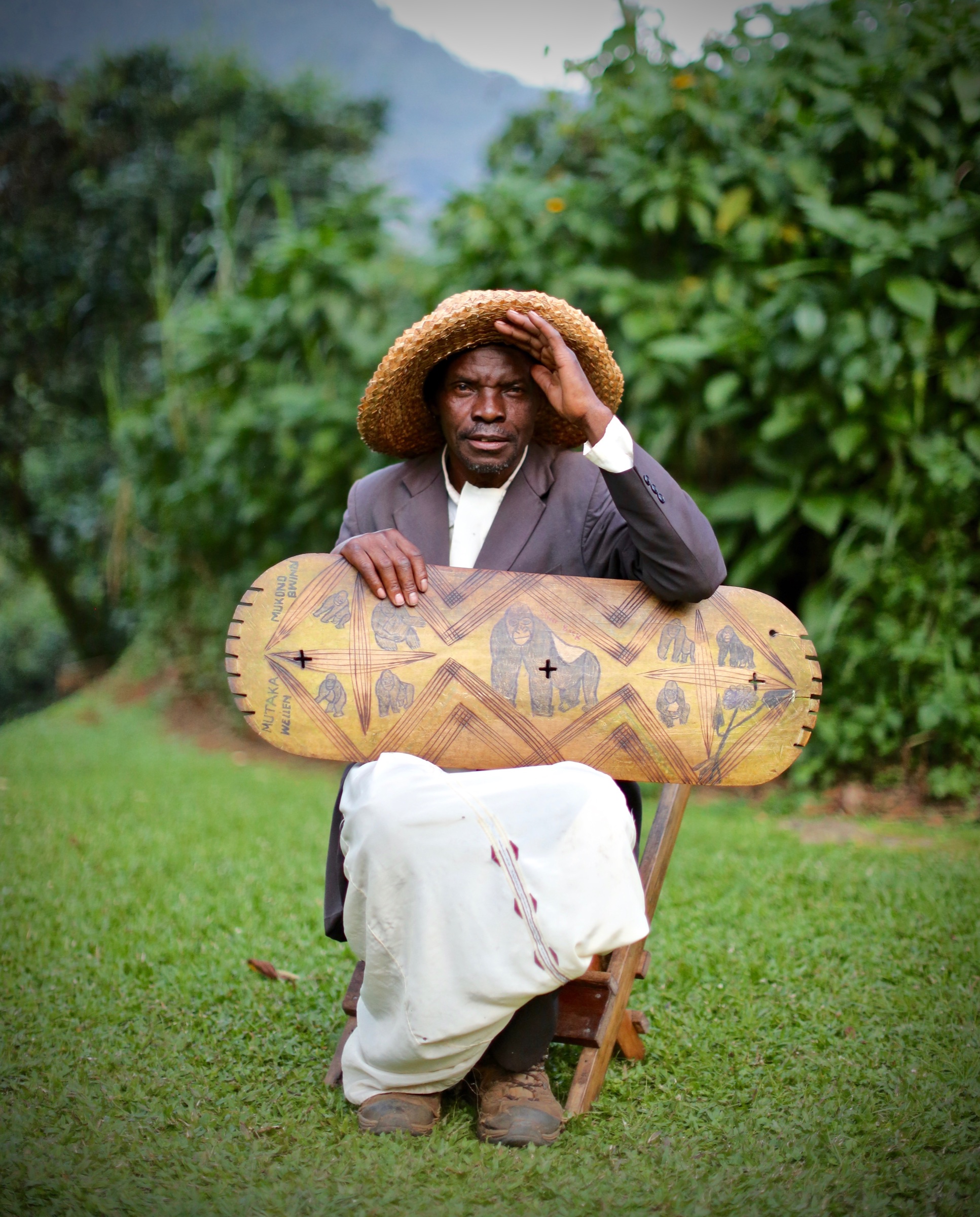 A Ugandan musician seated outdoors with a traditional harp